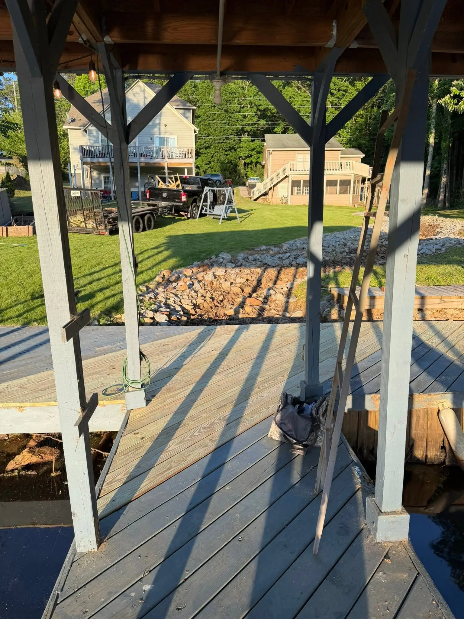 Dock repair under way beneath a covered boathouse, pry bars and a lumber trailer on the bank