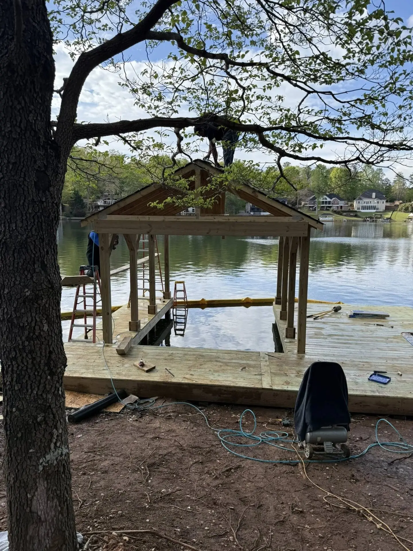 Crew framing a boathouse gable roof over a boat slip, lake estate homes in the background