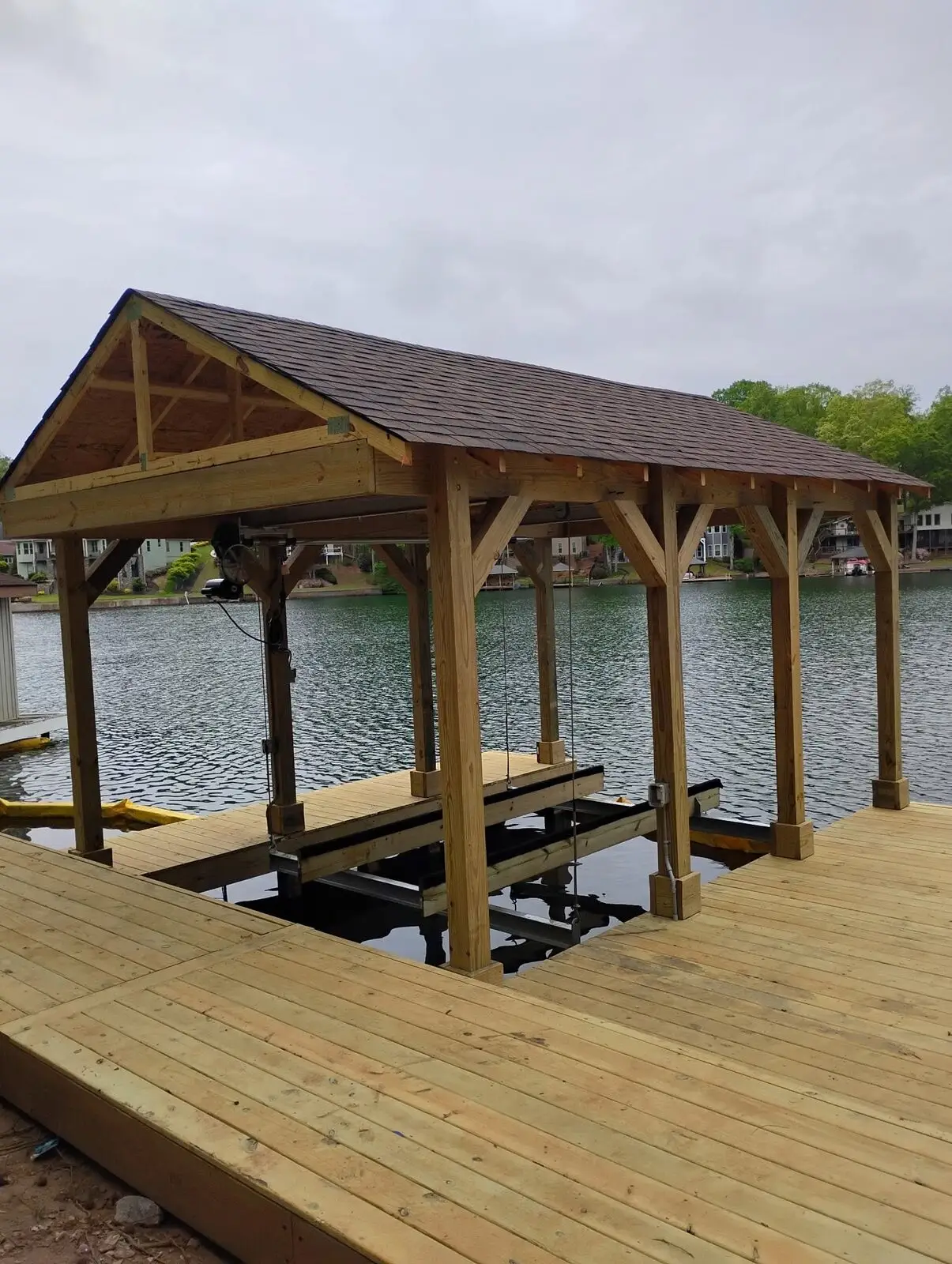 Covered boathouse with boat lift over the lake, dock deck unstained and rail not yet installed
