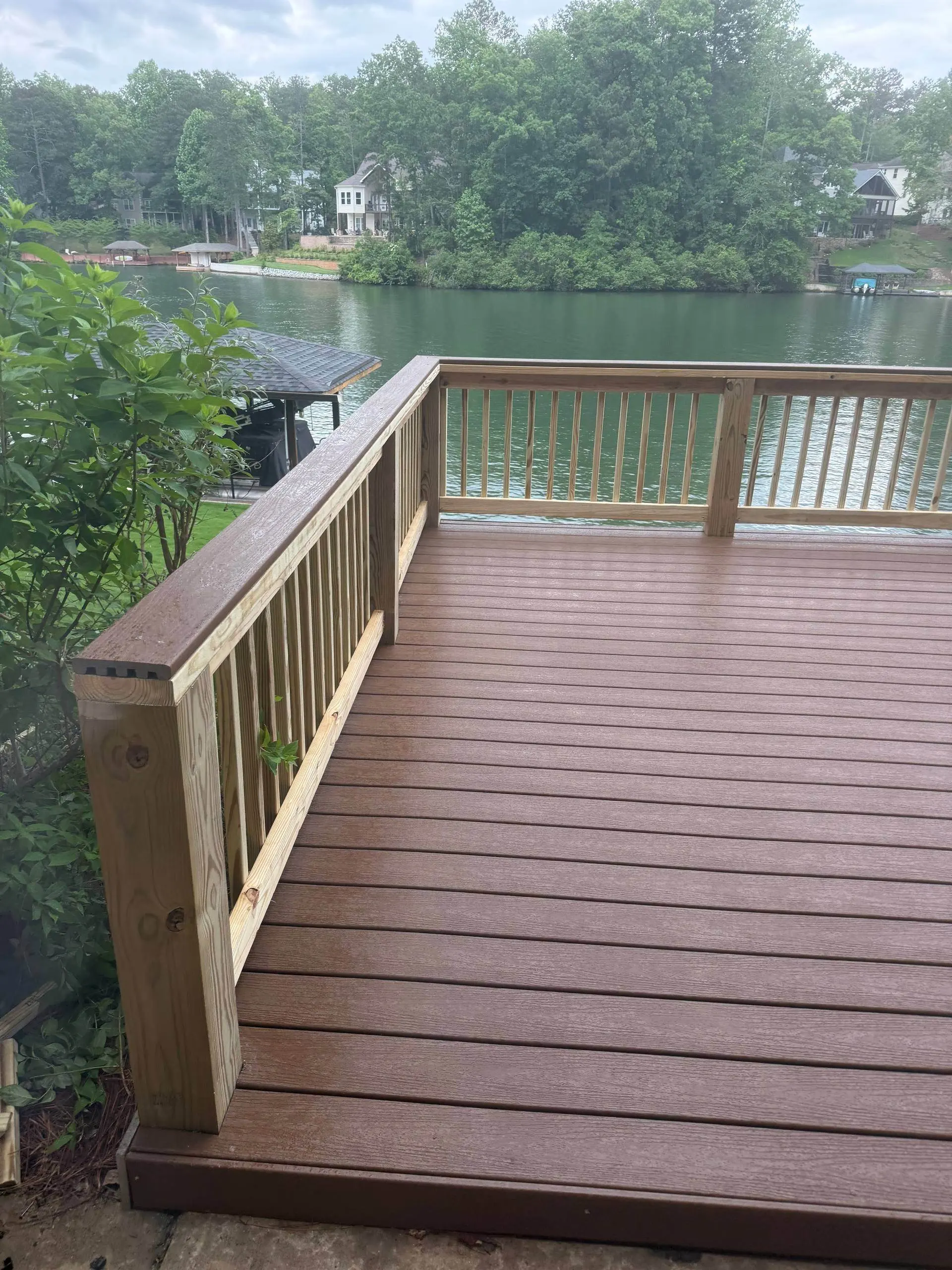 Finished composite deck with a wood rail overlooking the lake, covered boathouse dock and lakehouses across the water