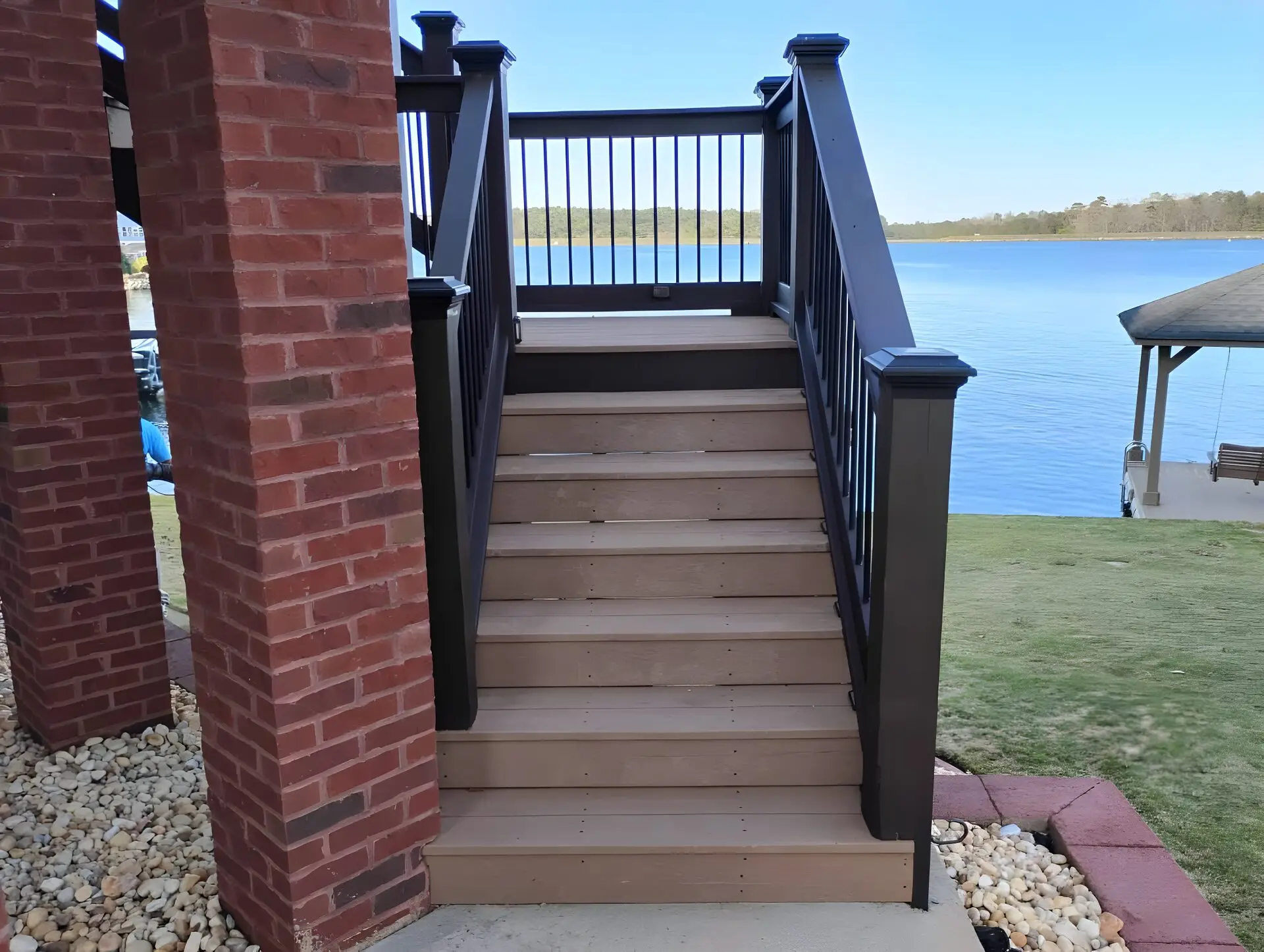 Composite deck stairs with dark-stained rail between brick columns, lake visible behind