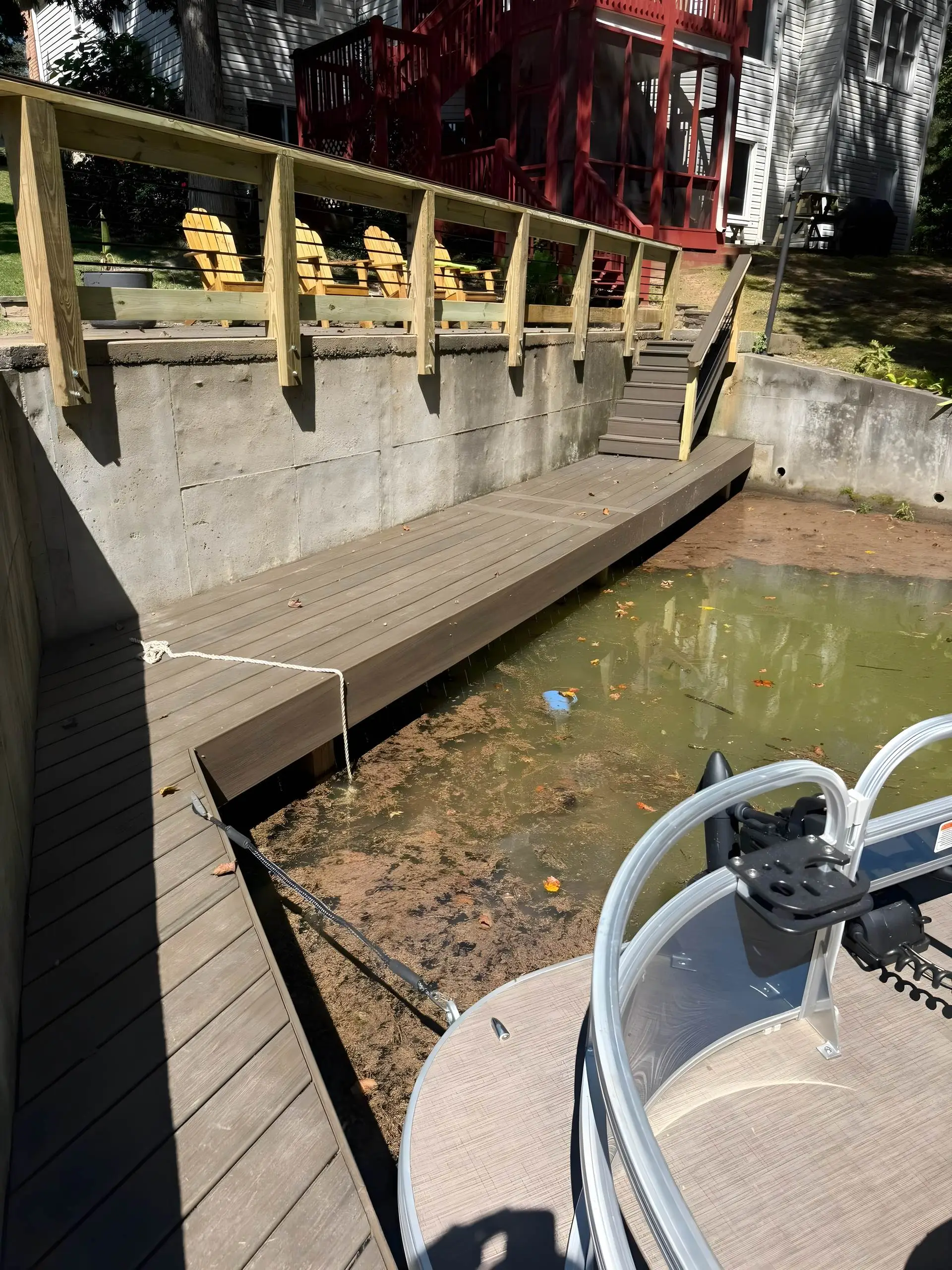 Composite dock built along a concrete seawall with a cable-rail terrace, Adirondack chairs, and pontoon boat