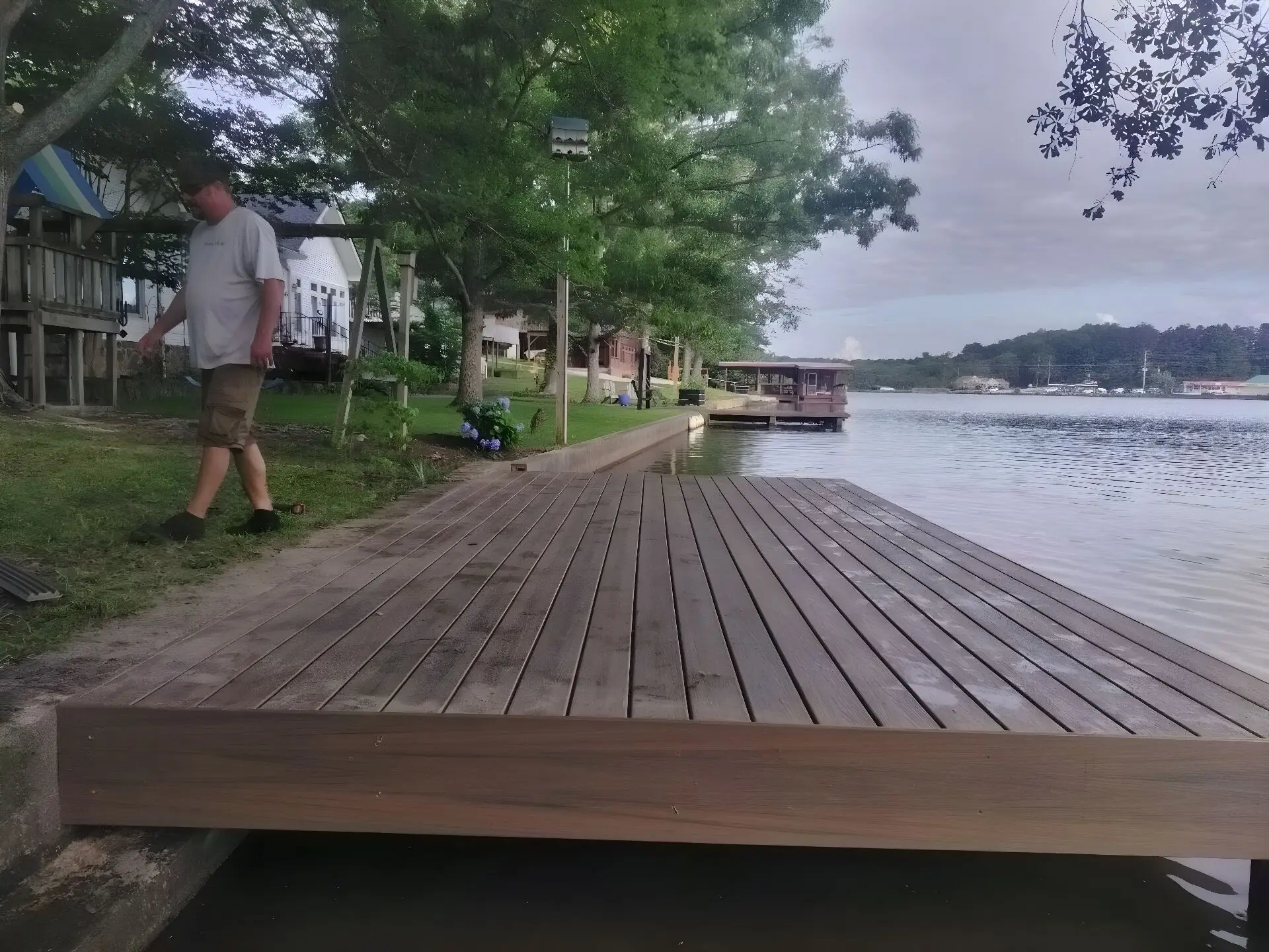 New composite dock platform at the water's edge with a covered dock further down the same shore and lake homes behind