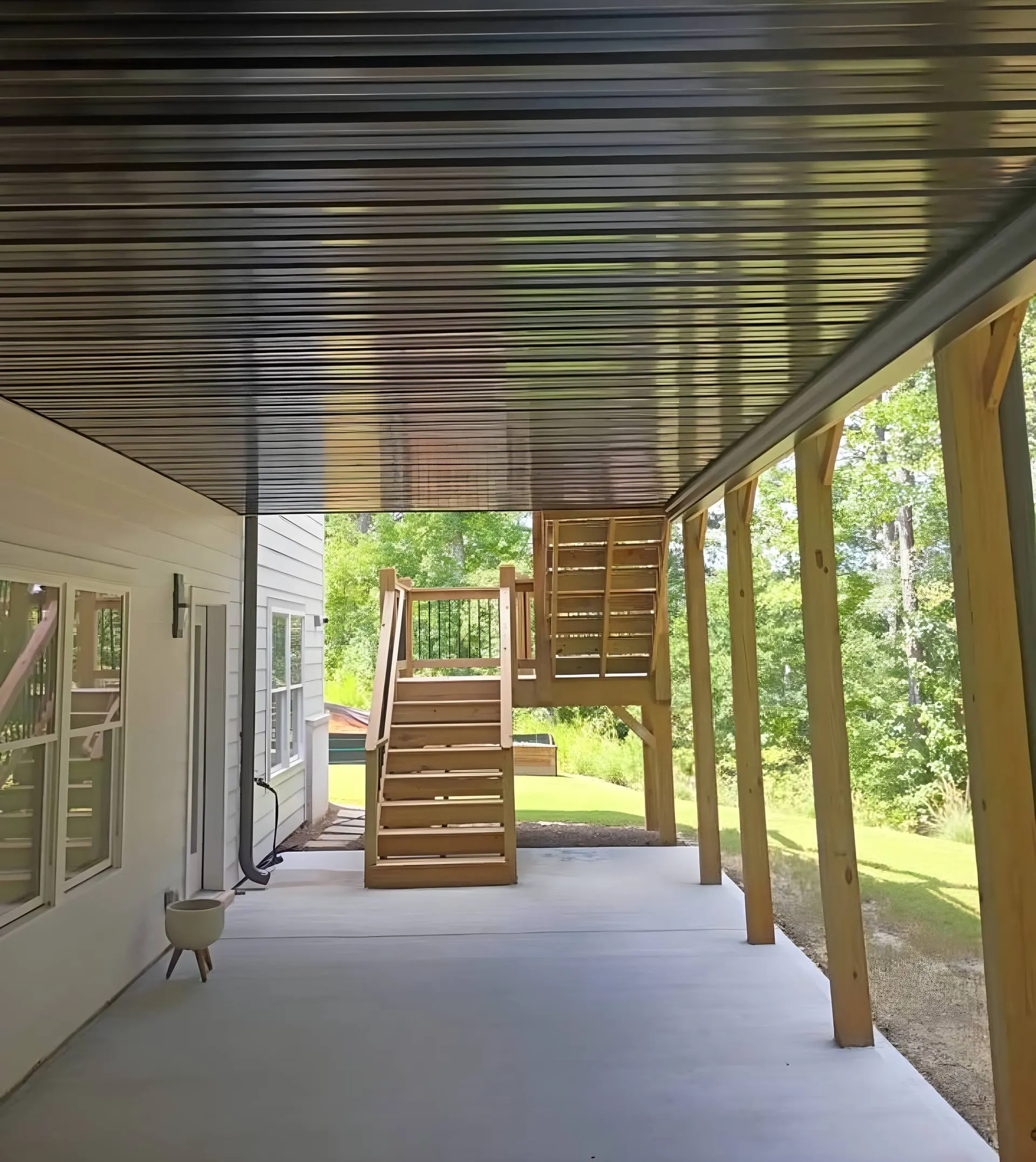 Finished covered patio addition with a black corrugated metal ceiling, new wood staircase, and poured concrete slab on the back of a home