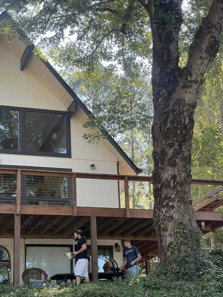 Crew building a redwood-stained wraparound deck with cable rail at an A-frame lake house