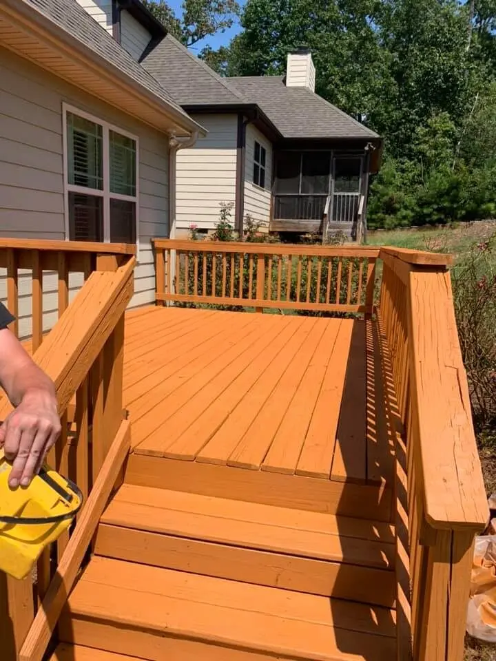 Hand applying deck stain from a pail onto fresh-toned boards