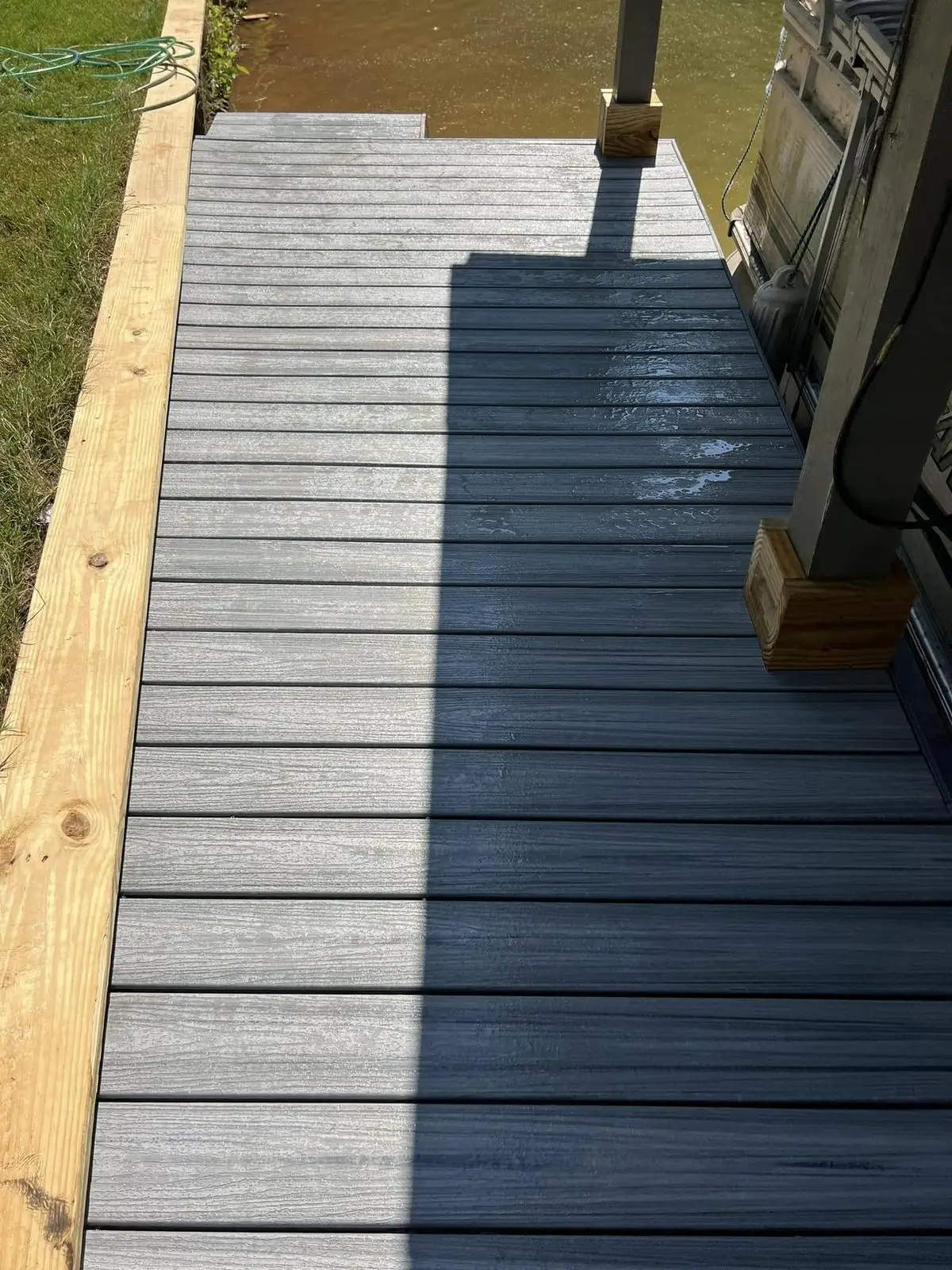 Gray composite decking freshly installed over the dock frame, pressure-treated border still raw, lake water below