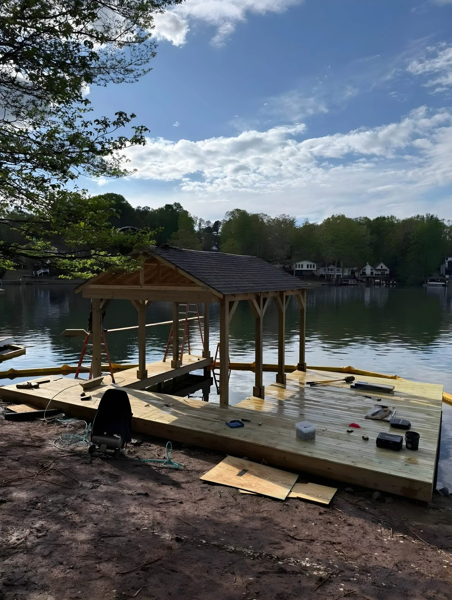 Boathouse/dock frame under construction: open sides with no walls or roof yet, bare unstained pressure-treated decking, tools and materials scattered on the deck.