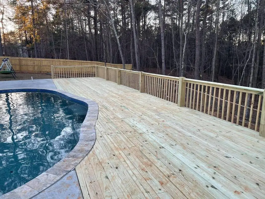 Wide pressure-treated pool deck curving around an in-ground pool at sunset