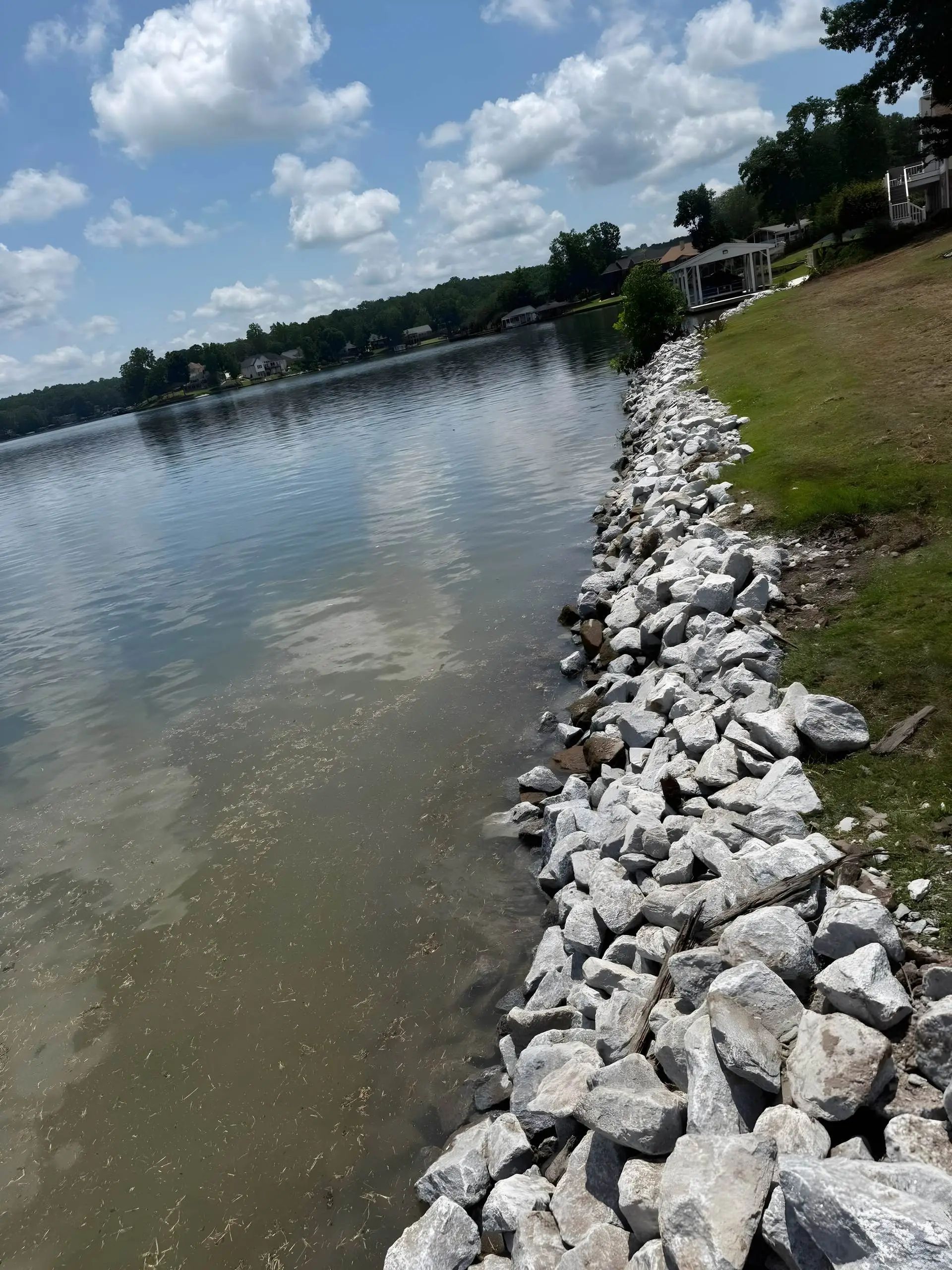 Rip-rap rock seawall along a lake shoreline with lakehouses in the distance