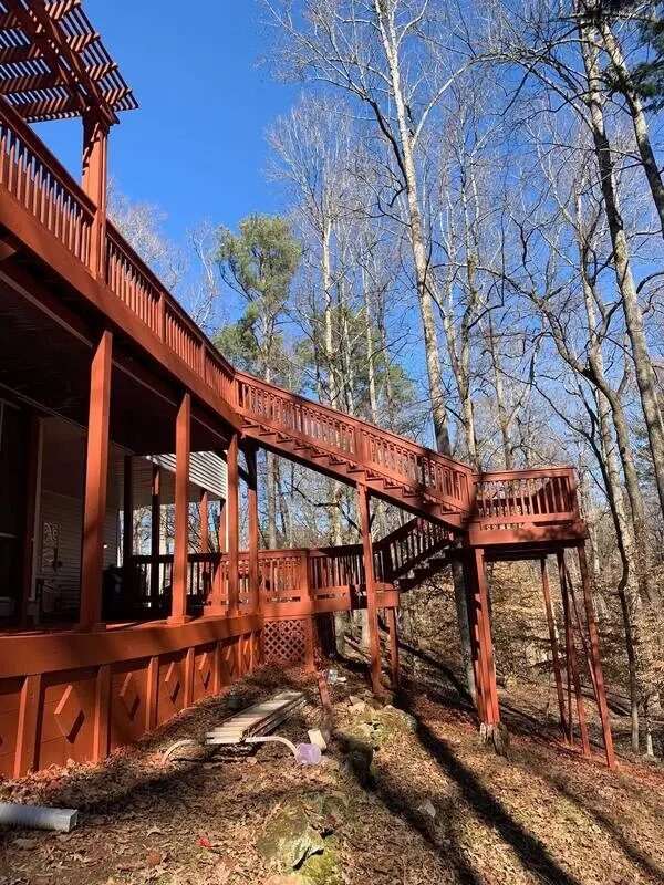 Long red-stained deck staircase descending from a pergola-topped deck down through the trees