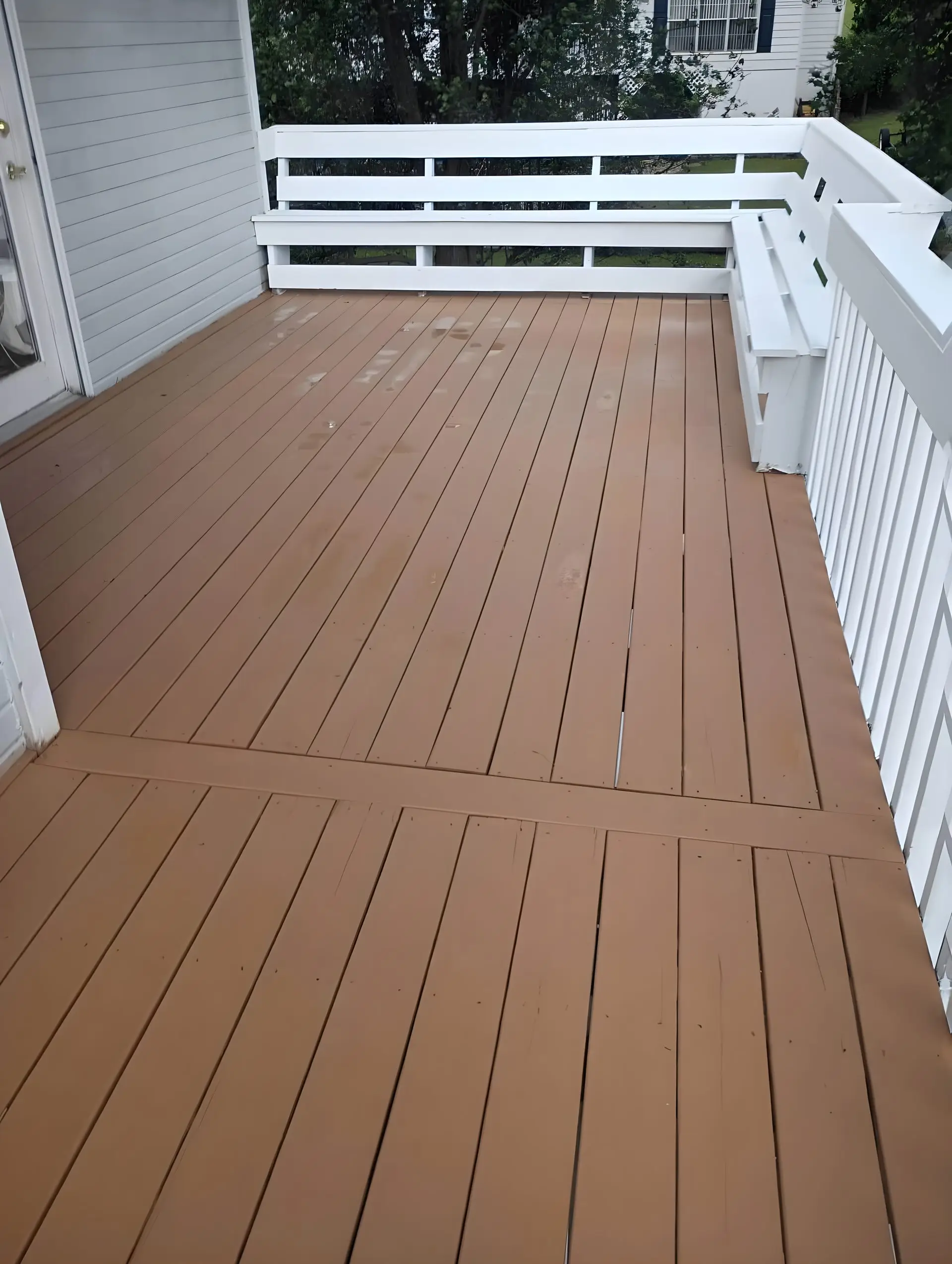 Finished stained deck corner with white rail and built-in bench seating, neighboring house visible beyond the rail.