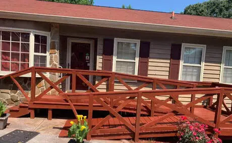 Red-stained ramp-style deck with cross-brace railings at a brick-front ranch home, flowers blooming along the walk