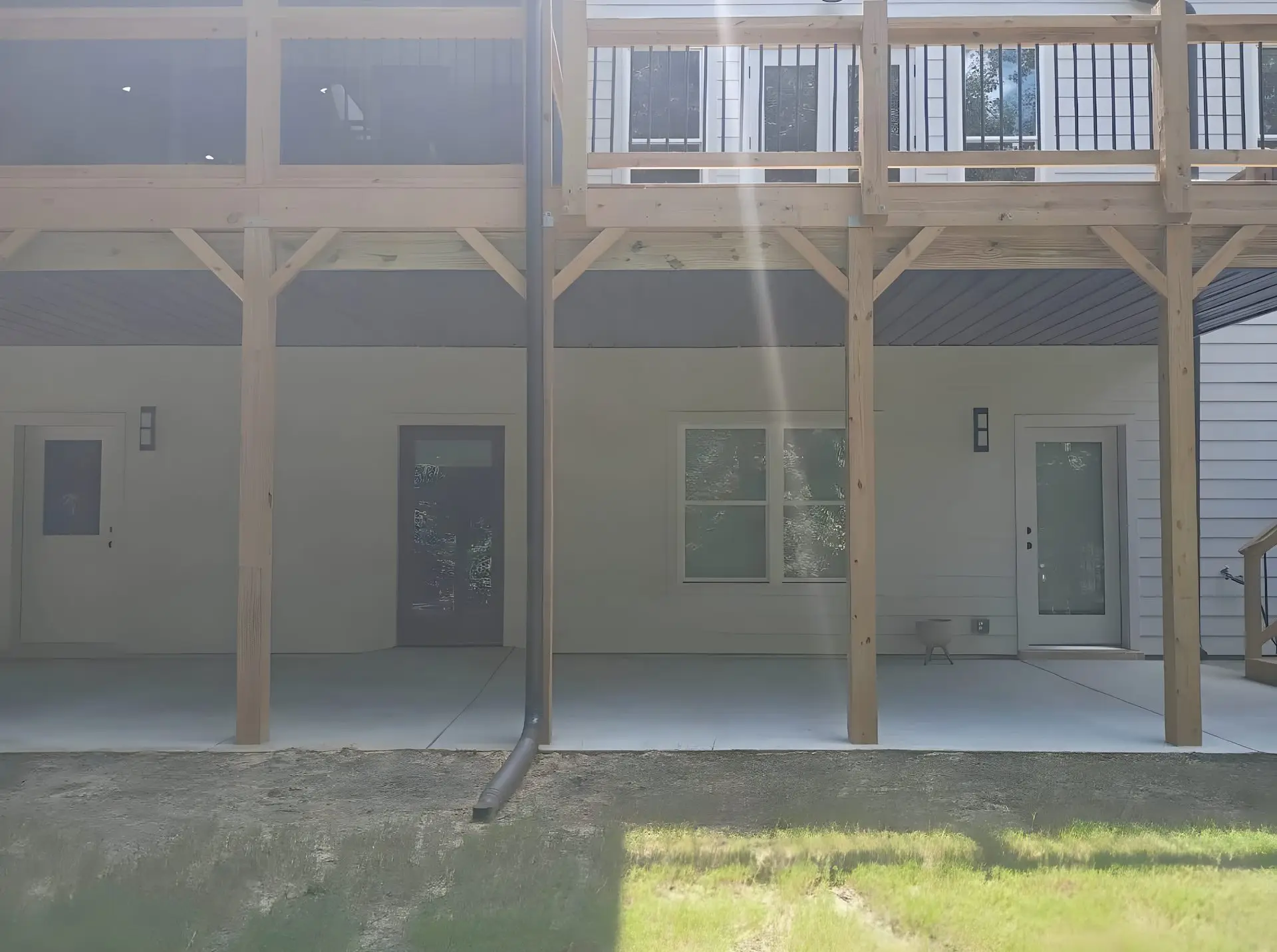 Full exterior of a two-story house showing the elevated deck above and covered patio below, walkout glass doors, concrete patio floor.