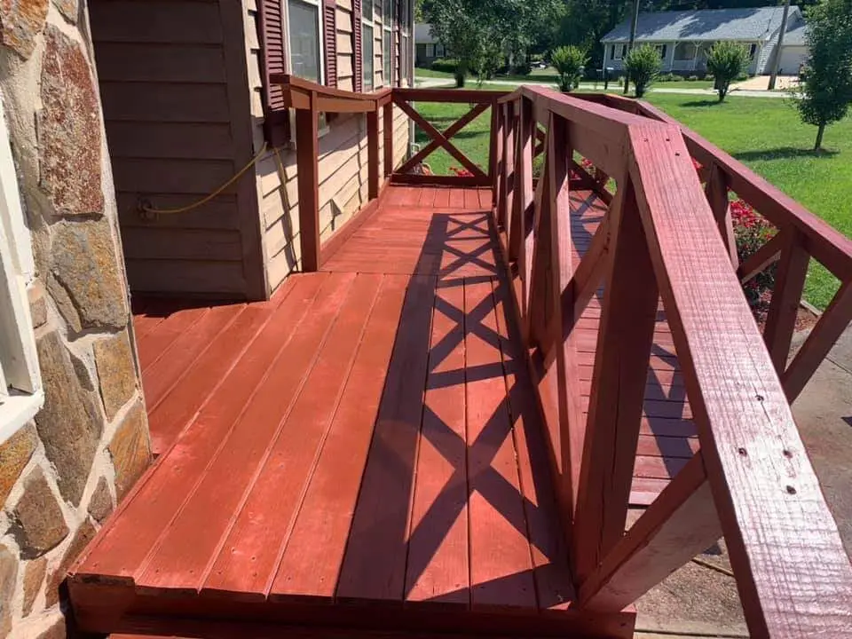 Red stained deck with an X pattern rail against a stone house facade and green lawn